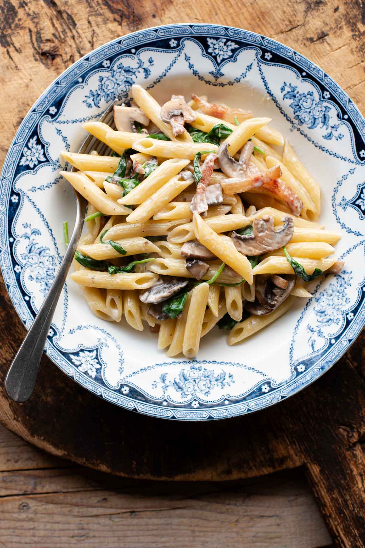 An overhead shot of mushroom spinach pasta in a blue and white bowl.