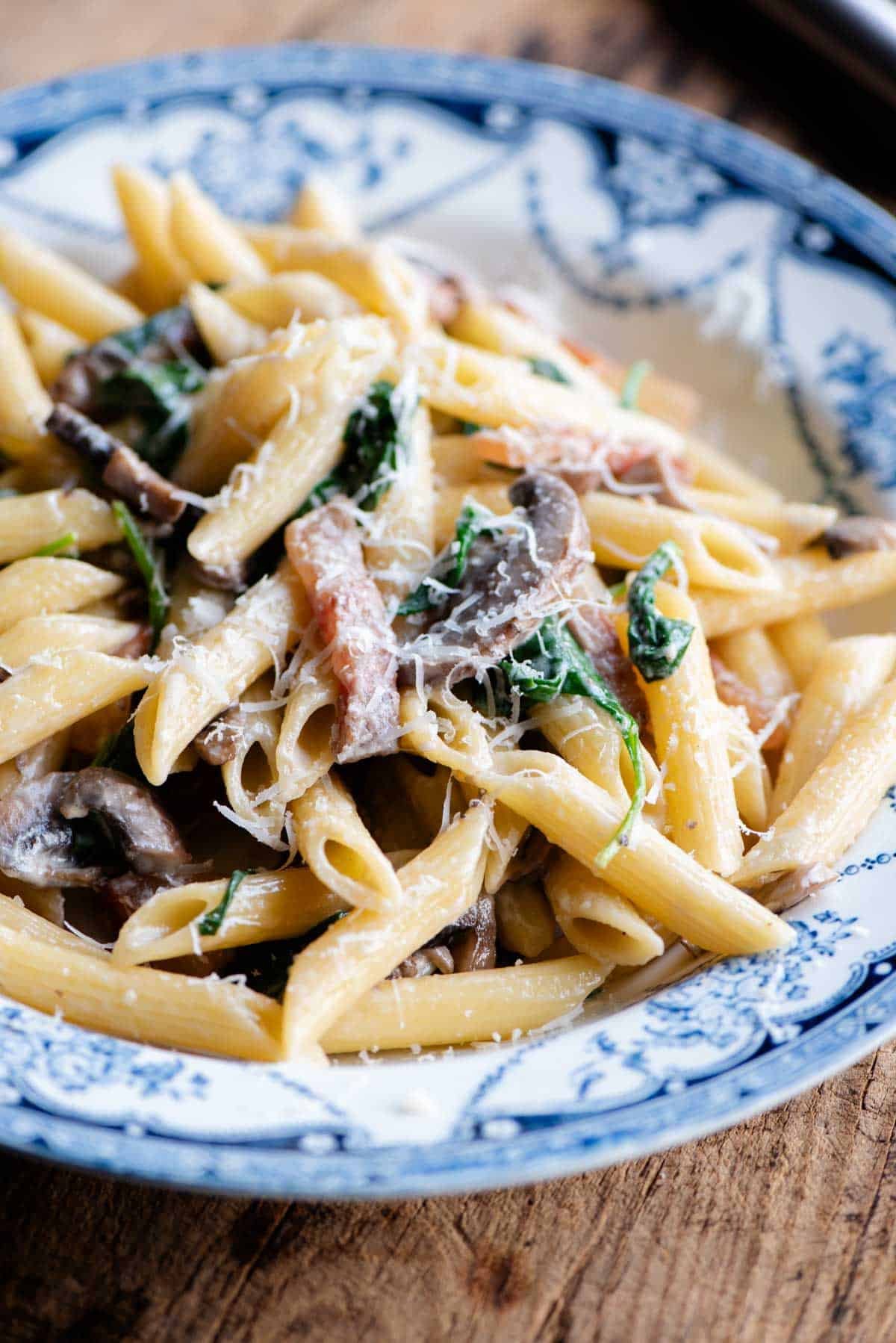 A close up of mushroom spinach pasta in a blue and white bowl.