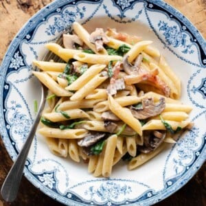 A cropped close up of mushroom spinach pasta in a blue and white bowl with a fork at the side.