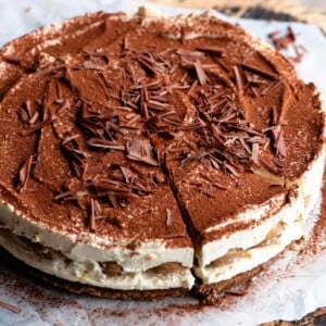 A close up of a tiramisu cheesecake on a wooden board dusted with cocoa powder.