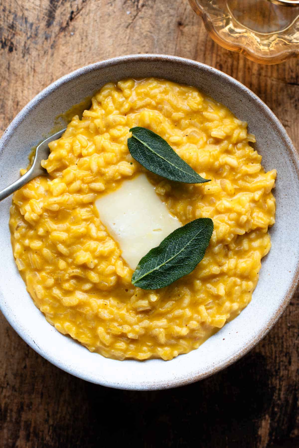 An overhead shot of a Pumpkin Risotto with a slice of Taleggio cheese and crispy sage on top.