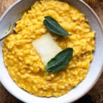An overhead shot of pumpkin risotto in a bowl with a slice of cheese and sage leaves on top.