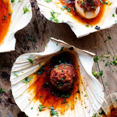 An overhead shot of scallops in their shells with a Nduja garlic butter on top.