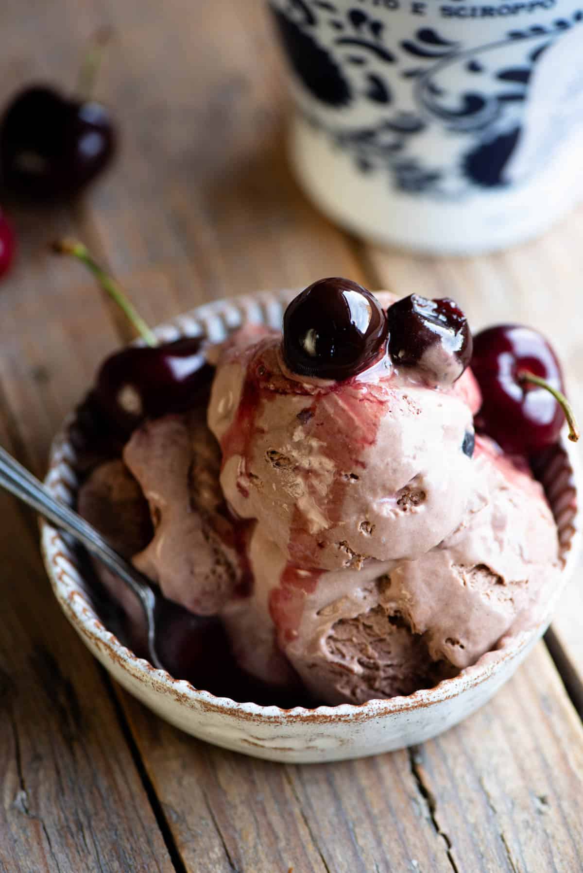 A close up of three scoops of cherry chocolate ice cream in a small dish topped with cherries.
