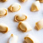 A close up cropped image of homemade Agnolotti on a wooden board.