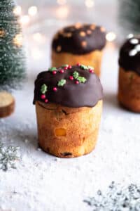 A mini Panettone dipped in melted chocolate sitting on a snowy Christmas themed surface with Christmas trees at the side.