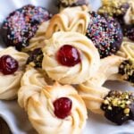 A close up of Italian butter cookies on a plate. In the centre is a round cookie with a candied cherry on top.