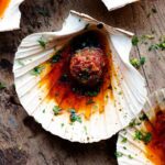 A close up of a scallop in a shell topped with nduja garlic butter.
