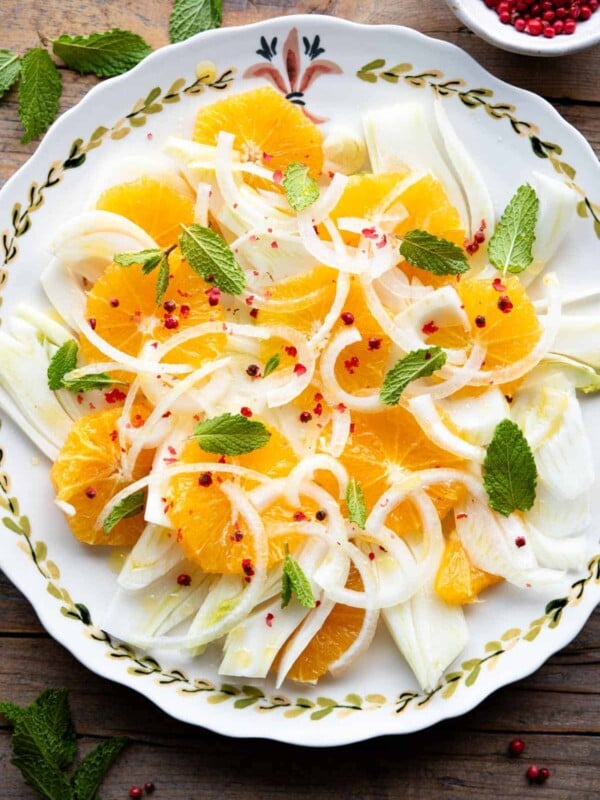 An overhead shot of a fennel and orange salad on a plate topped with mint leaves and pink peppercorns.