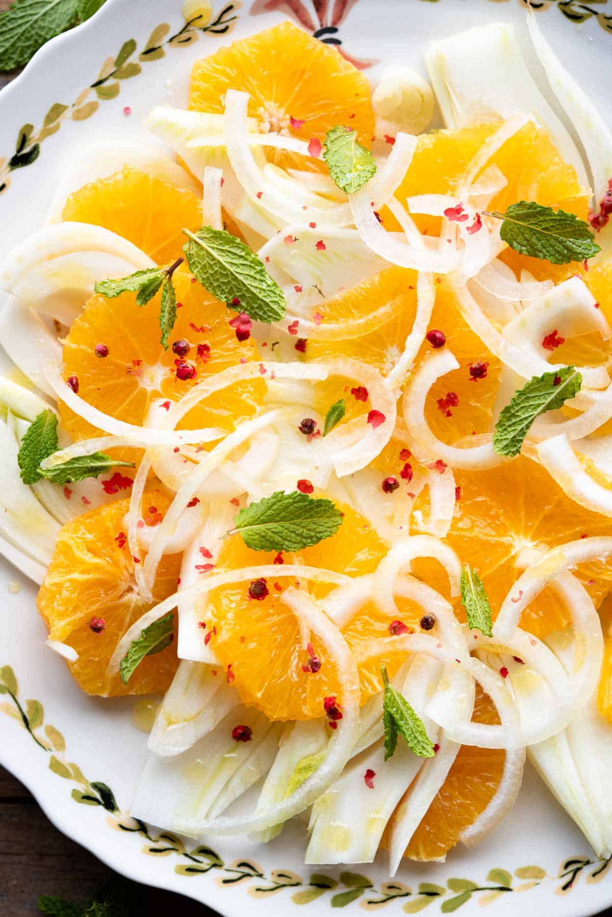 A close up of a fennel orange salad with white onion, mint leaves and pink peppercorns.