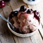A close up of Amarena cherry chocolate ice cream scoops in a small bowl on a wooden surface.