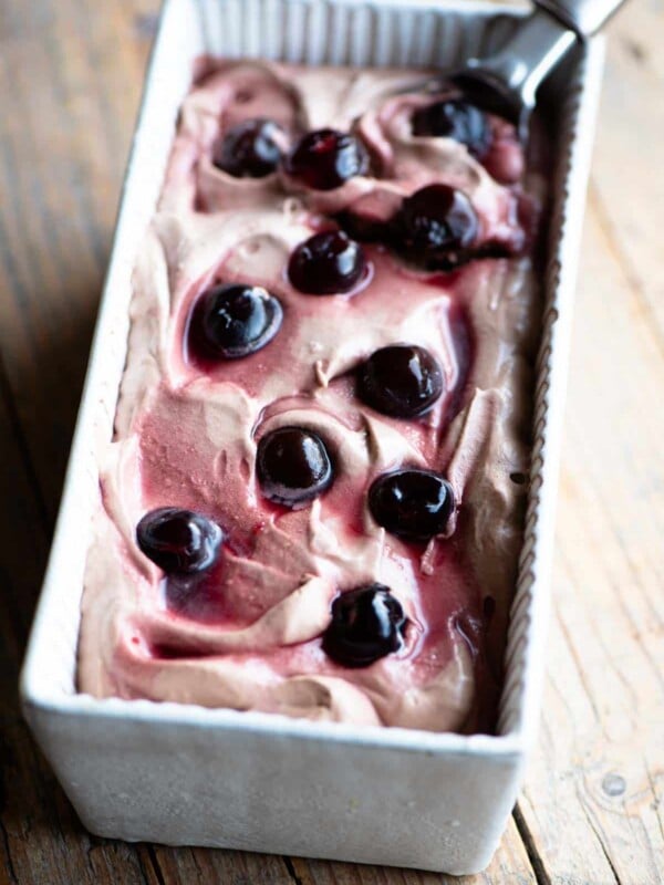 Cherry chocolate ice cream in an ice cream dish with an ice cream scoop at the side.