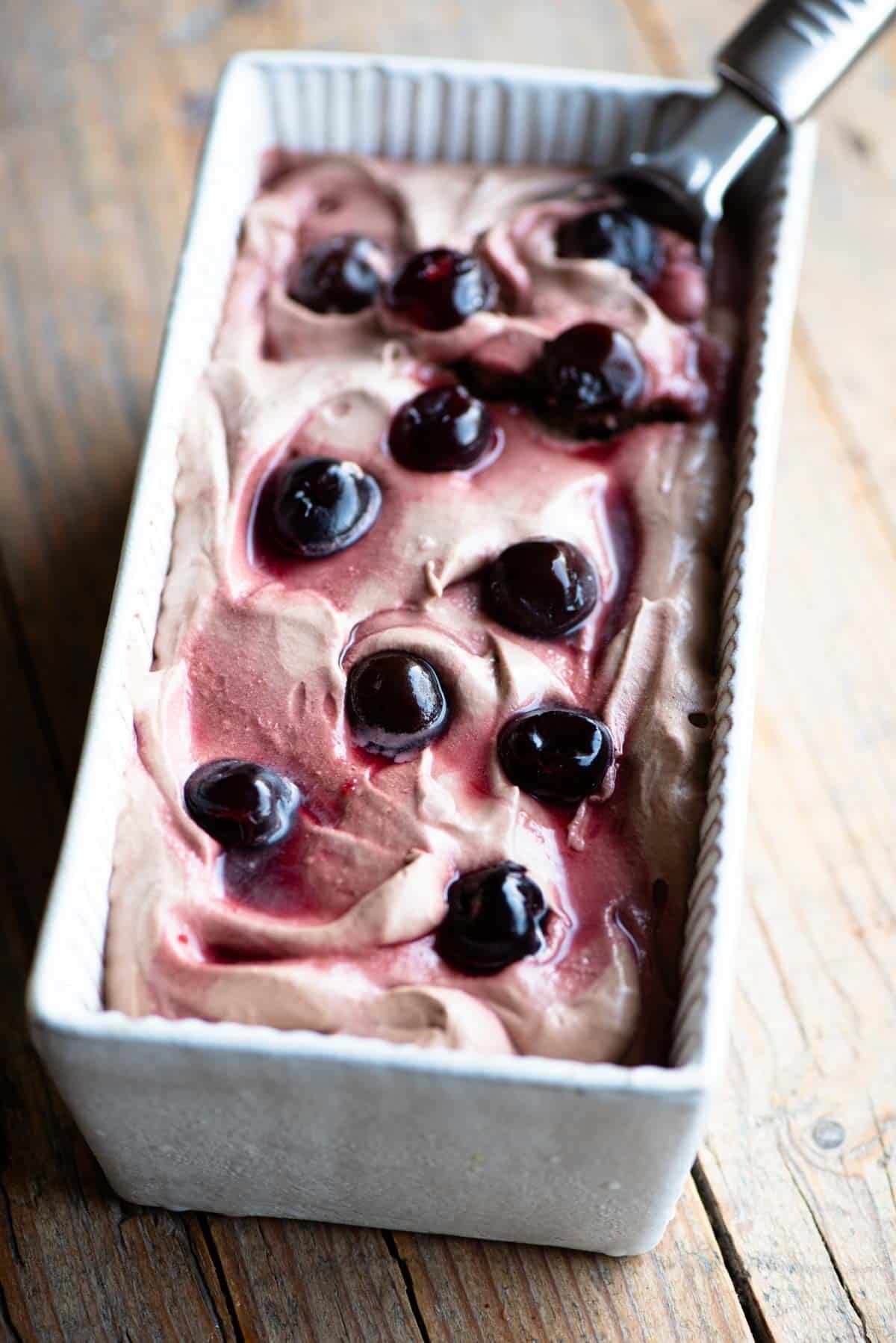 Cherry chocolate ice cream in an ice cream dish with an ice cream scoop at the side.