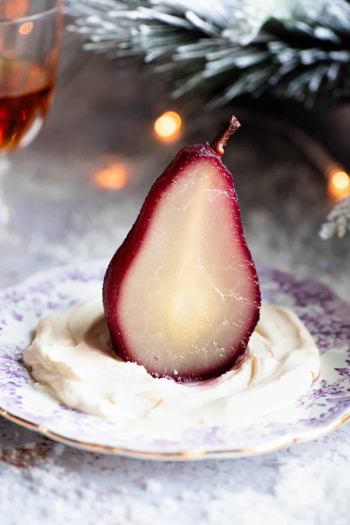 A red wine poached pear cut in half on a plate with Amaretto whipped cream, the background is Christmassy.
