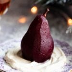 A close up of a red wine poached pear on top of amaretto whipped cream on a small dessert plate.