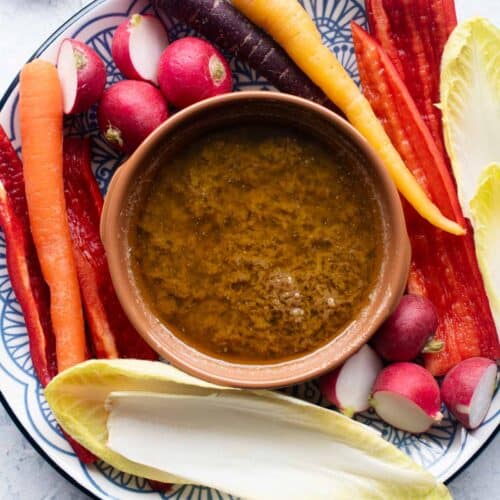 An overhead shot of Bagna Cauda in a terracotta dish with raw vegetables around it.