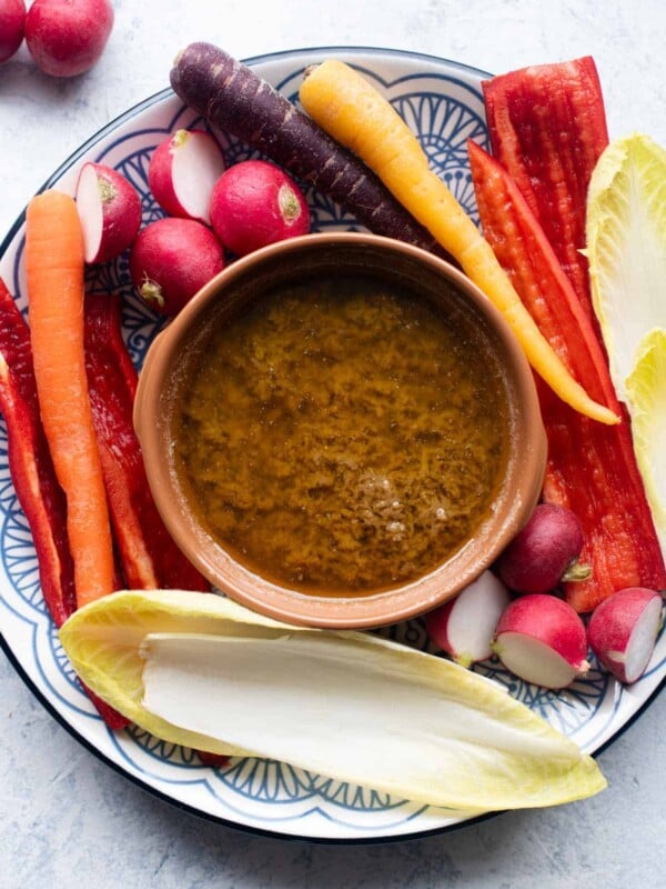An overhead shot of Bagna Cauda in a terracotta dish with raw vegetables around it.