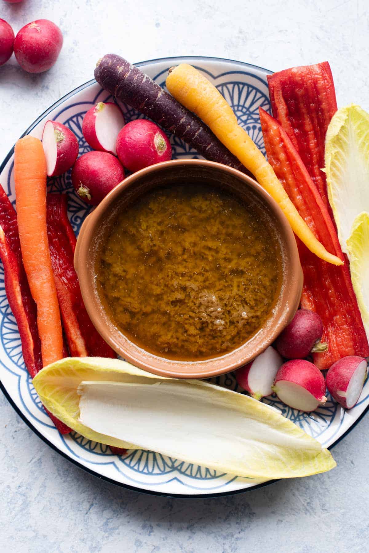 An overhead shot of Bagna Cauda in a terracotta dish with raw vegetables around it.