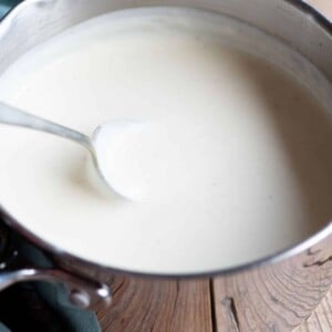 Italian Besciamella sauce in a pot with a spoon. The background is wooden.