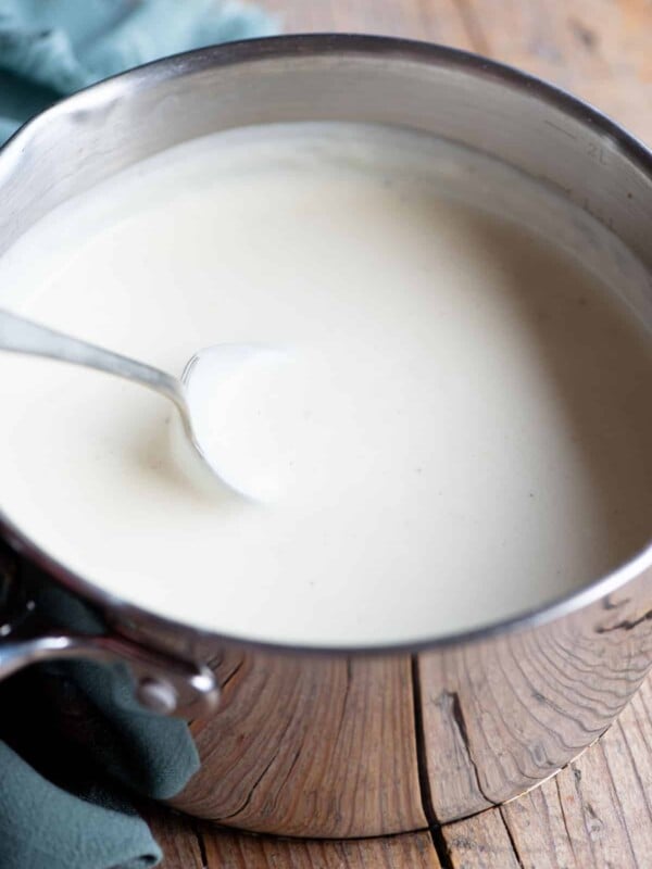 Italian Besciamella sauce in a pot with a spoon. The background is wooden.