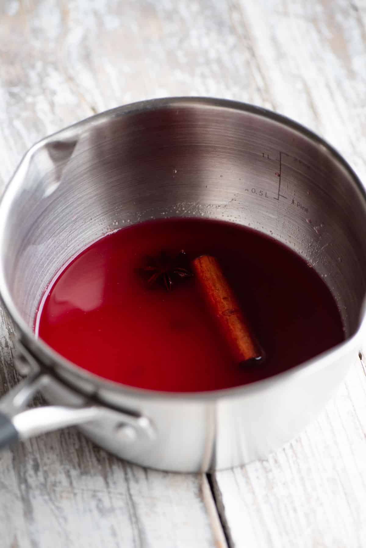 A small pot with cranberry juice and Christmas spices inside sitting on a white wooden table.