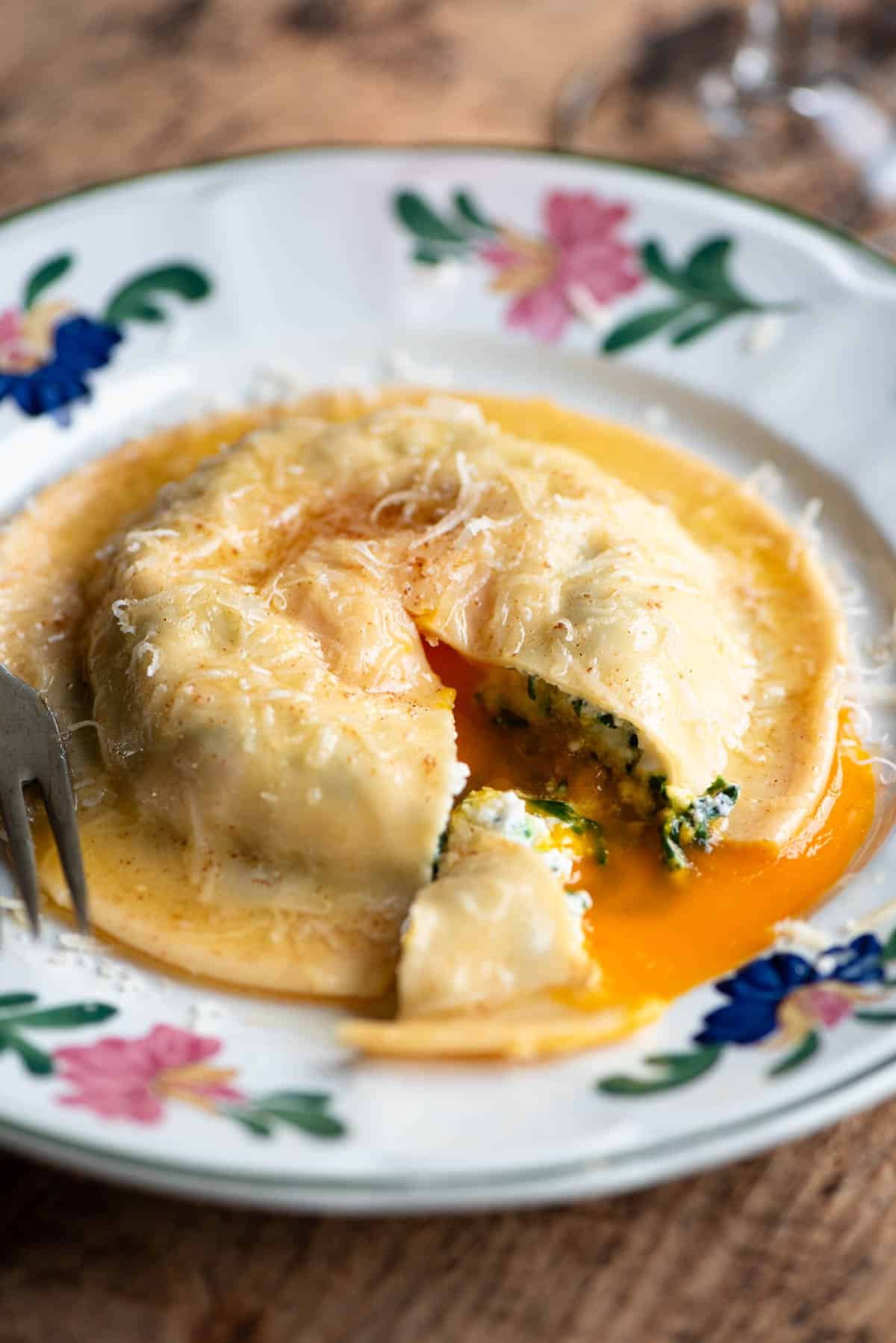 A close up of an egg yolk ravioli on a plate cut open with egg yolk running out.