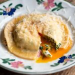 A close up cropped image of egg yolk ravioli cut open with egg yolk running out.