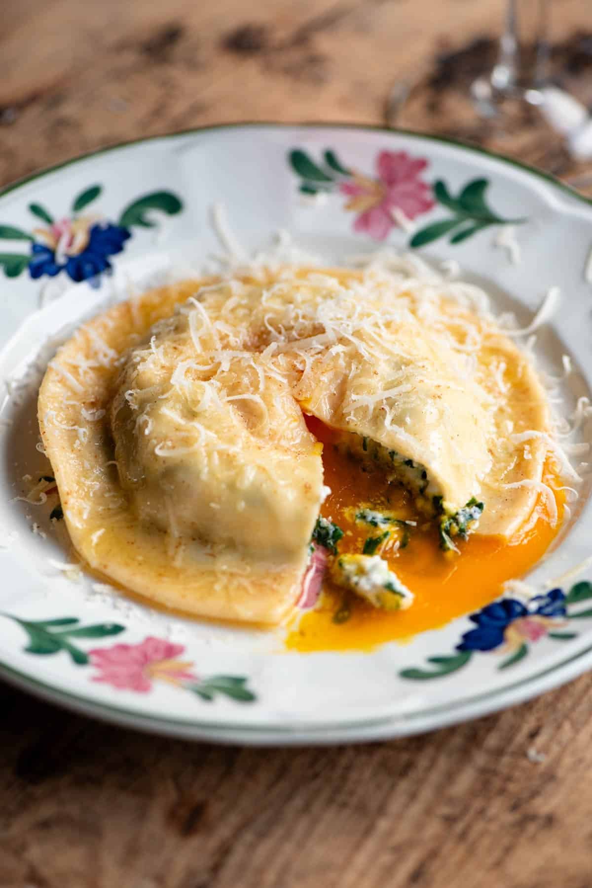 A close up of an egg yolk ravioli cut open on a plate with egg yolk oozing out.