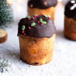 A close up of a mini Panettone topped with melted chocolate and Christmas sprinkles.