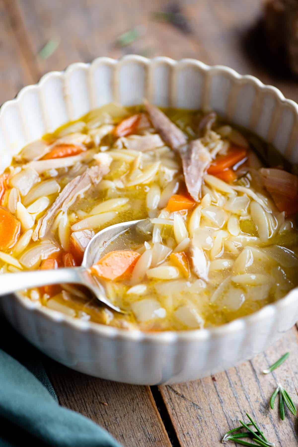 A close up side shot of lemon chicken orzo soup in a bowl with a spoon.