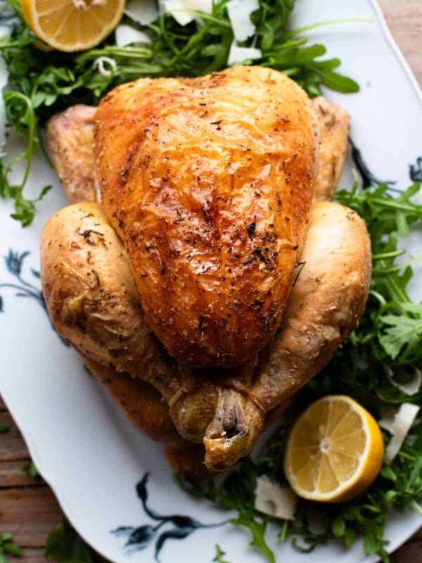 An overhead shot of a lemon roast chicken on a serving plate with arugula and lemon slices at the side.