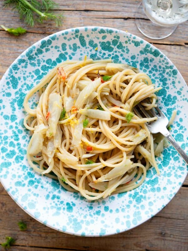 An overhead shot of roasted fennel pasta in a blue spotted bowl sitting on a rustic wooden surface.