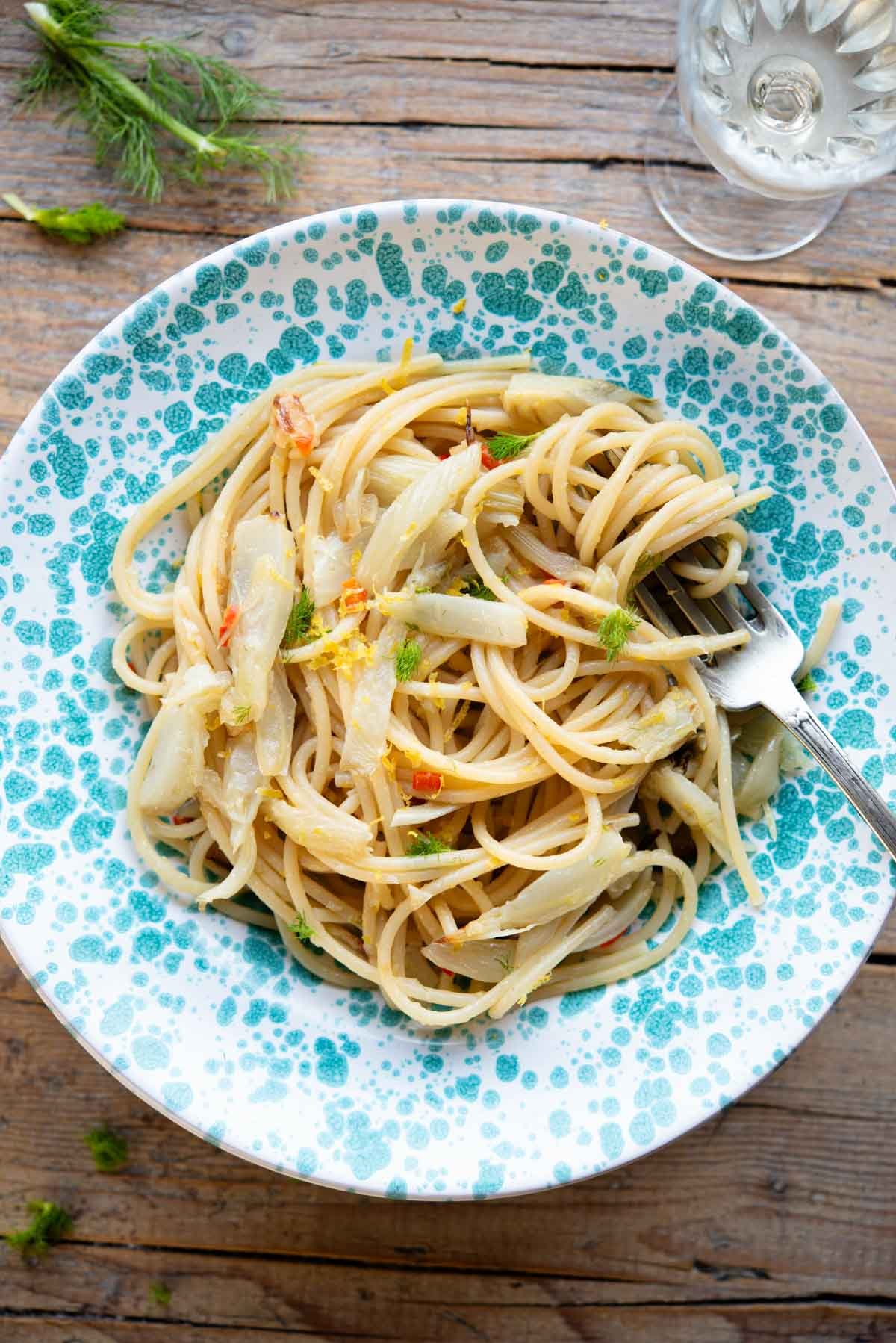 An overhead shot of roasted fennel pasta in a blue spotted bowl sitting on a rustic wooden surface.