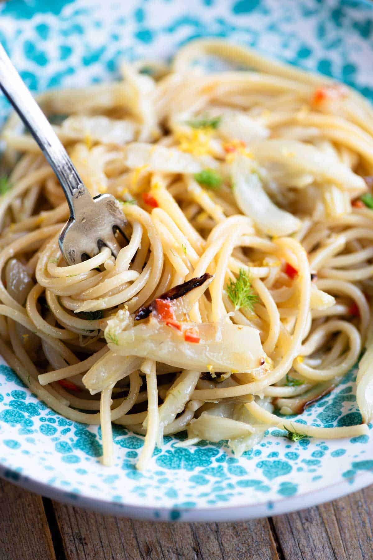 A close up of roasted fennel spaghetti in a bowl twirled around a fork.