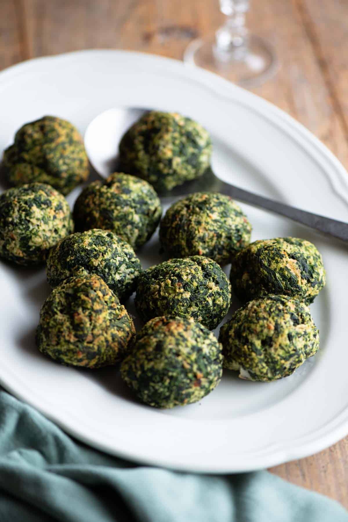 Baked spinach balls on a white serving plate with a serving spoon.