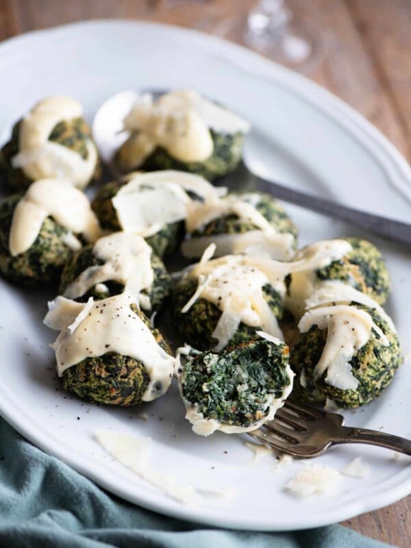 Spinach balls on a white serving plate with parmesan cream. One is cut open on a fork.