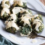 A close up of spinach balls on a white serving plate drizzled with Parmigiano cream.