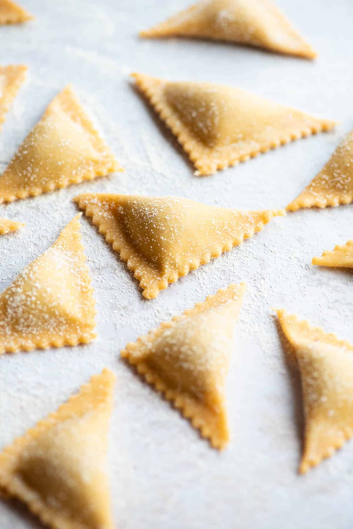 A close up side shot of fresh Triangoli pasta on a light grey coloured board.