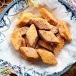 A square image of Crema Fritta (fried custard bites) in a bowl sitting on a wooden surface.