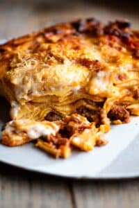 One slice of lamb lasagna on a plate sitting on a wooden surface.