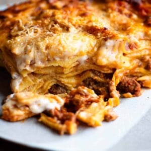 One slice of lamb lasagna on a plate sitting on a wooden surface.