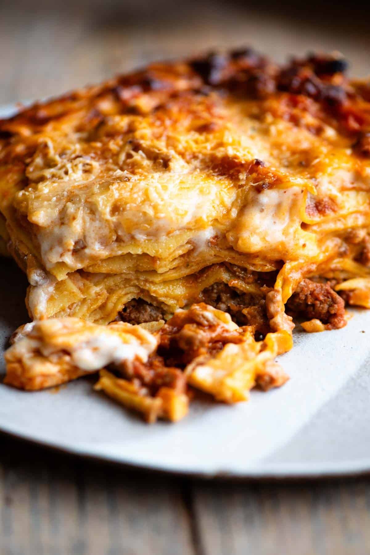 One slice of lamb lasagna on a plate sitting on a wooden surface.