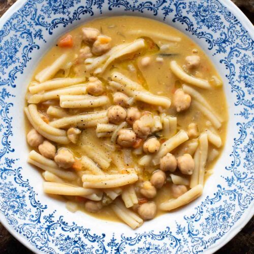 An overhead shot of pasta e ceci (psta and chickpeas) in a blue bowl on a wooden surface.
