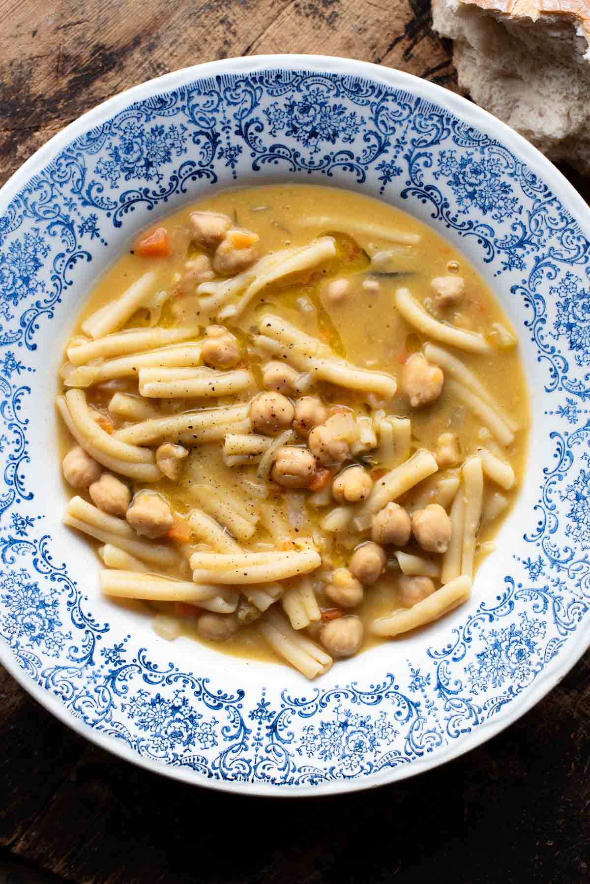 An overhead shot of pasta e ceci (psta and chickpeas) in a blue bowl on a wooden surface.