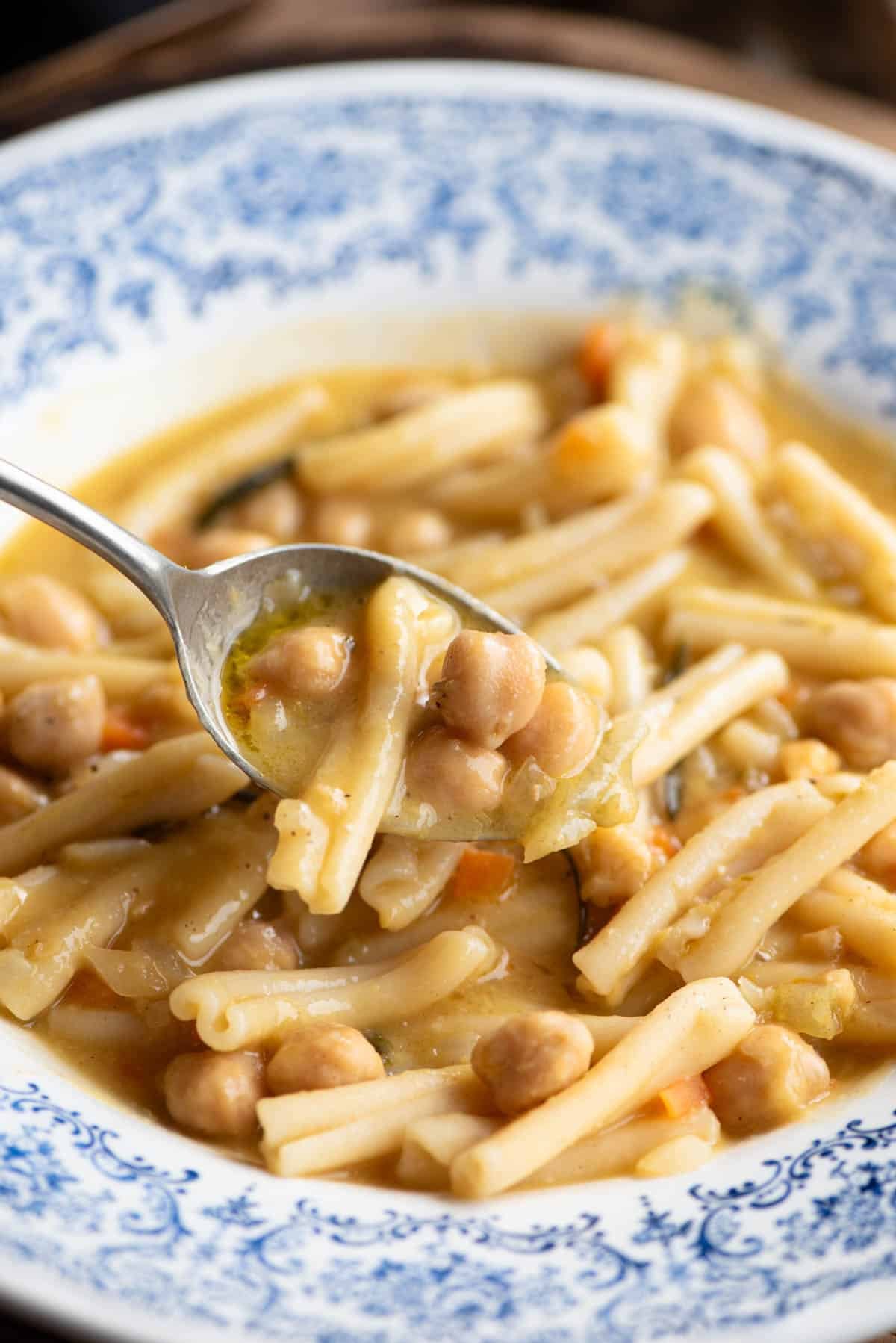 A close up of a spoonful of pasta and chickpeas over a blue bowl.