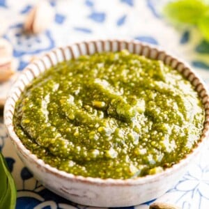 Pistachio pesto in a small round dish sitting on a blue patterned board.