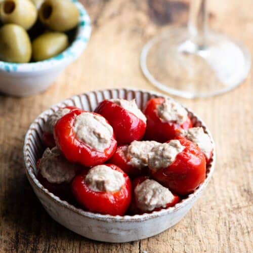 Tuna stuffed cherry peppers in a small dish with olives and a glass of wine at the side.