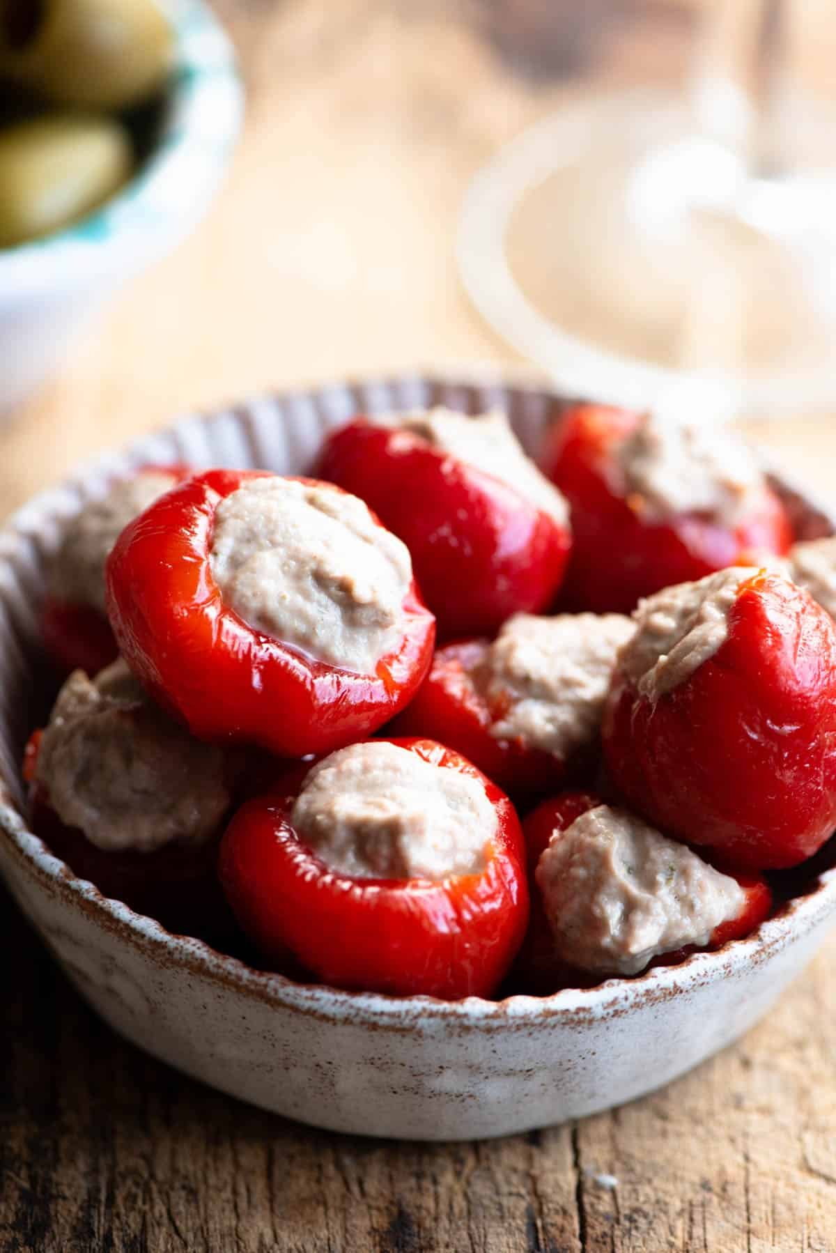 A close up of tuna stuffed cherry peppers in a small dish sitting on a wooden surface.