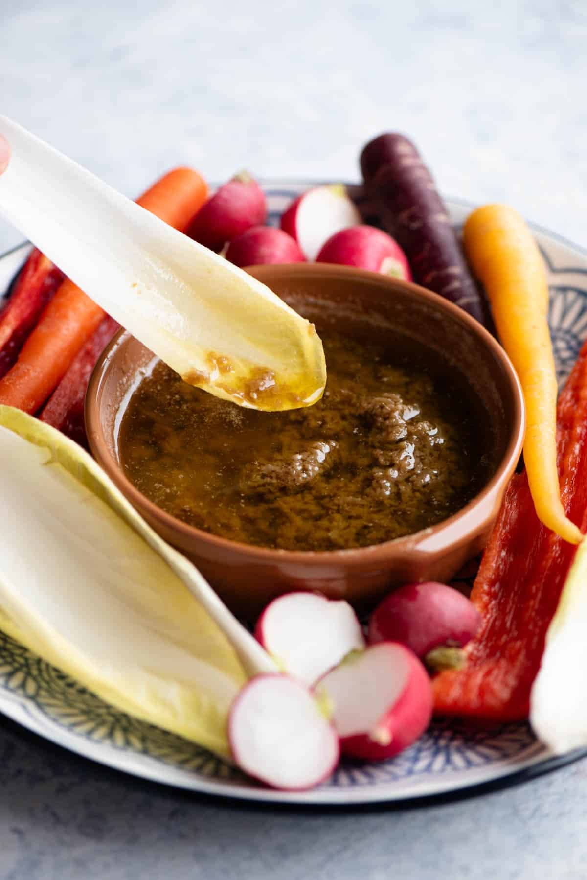 A close up of a piece of chicory being dunked into a Bagna Cauda dip.