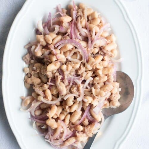 An overhead shot of cannellini beans, tuna and onion on a white platter.